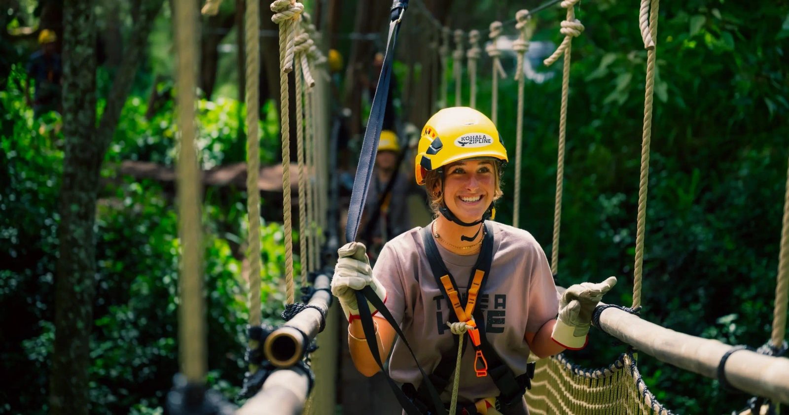 Smiling guest in a Kohala Zipline helmet, harnessed up on a rope sky bridge in the forest.