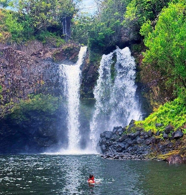 Guest swimming in the pool at the base of a twin waterfall on Hawaii Island.