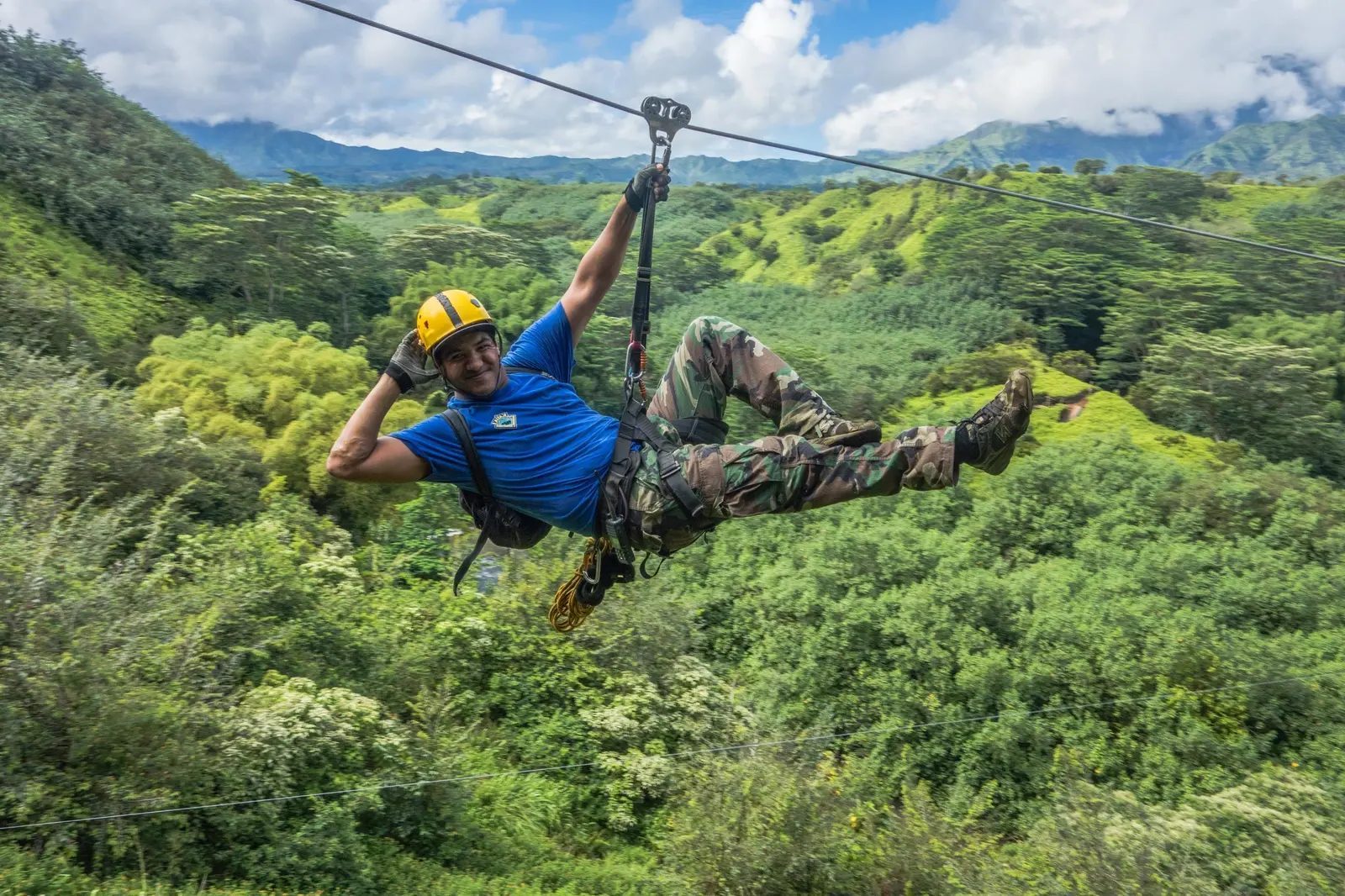 Guest ziplining high above a lush green valley with Mt. Waiʻaleʻale's misty peaks in the background, Kauaʻi