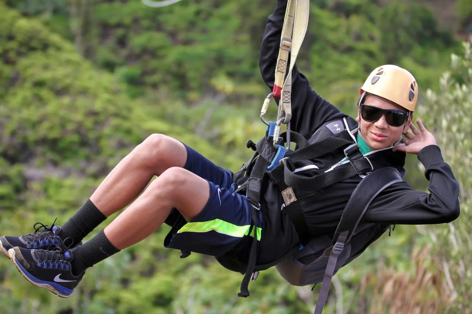 Guest in a yellow helmet smiling while ziplining over tropical forest on the Backcountry Zipline Tour, Kauaʻi