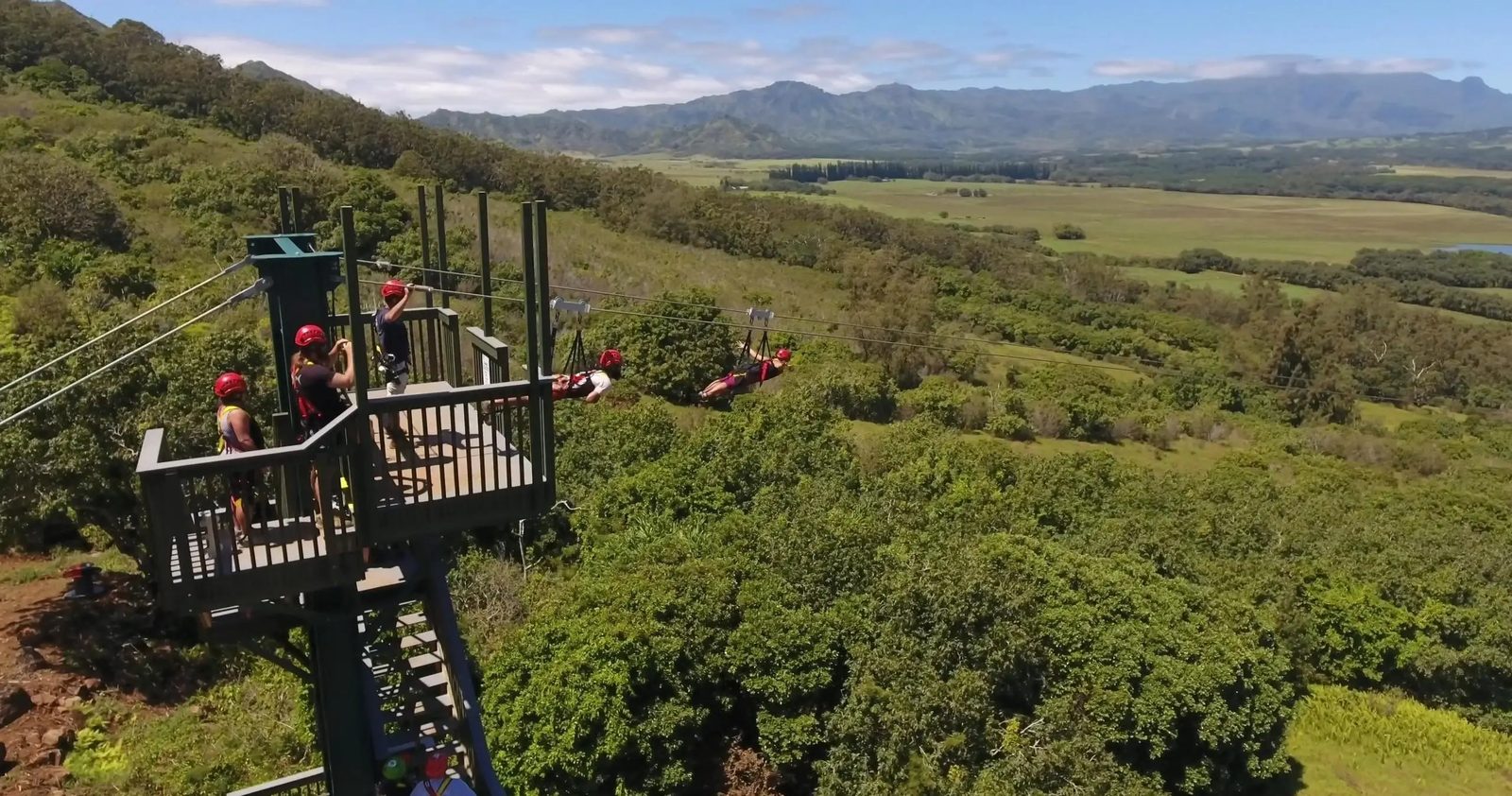 Aerial view of guests launching from the FlyLine tower and flying tandem over Kipu Ranch's green valley, Kauaʻi.