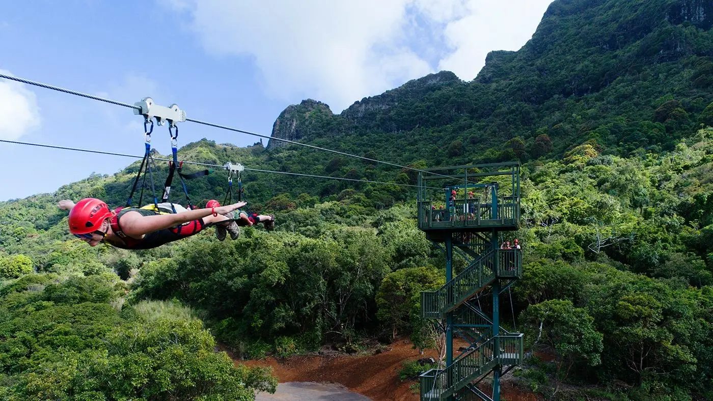 Flyer soaring past the FlyLine launch tower with the Hāʻupu Mountain Range rising behind, Kauaʻi.