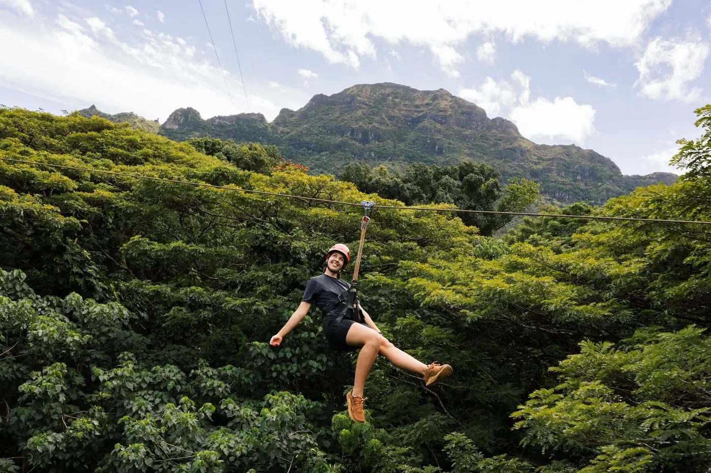 Guest ziplining over the treetops with the Haʻupu Mountain Range rising in the background at Kīpū Ranch, Kauaʻi.