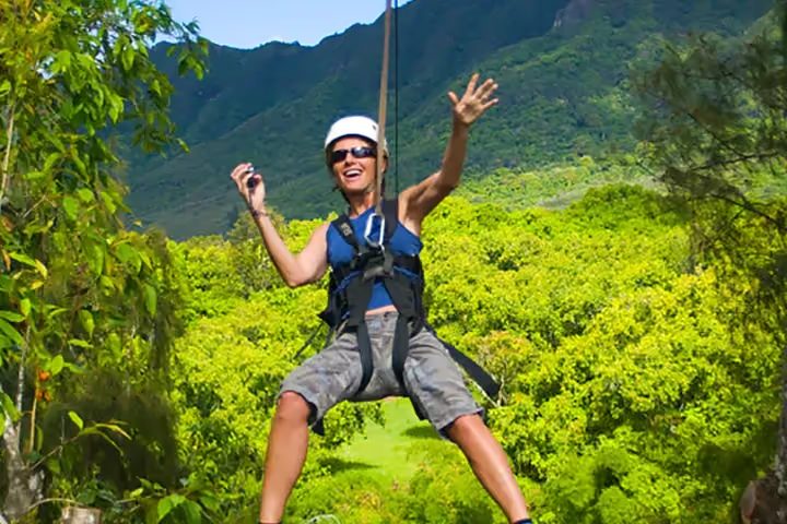 Guest smiling with arms raised while ziplining above the jungle canopy at Kīpū Ranch, Kauaʻi.