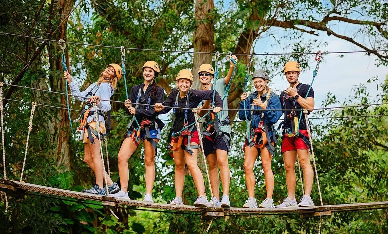 Group of guests in helmets and harnesses posing on a tree-to-tree suspension bridge on the NorthShore Zipline Tour, Maui