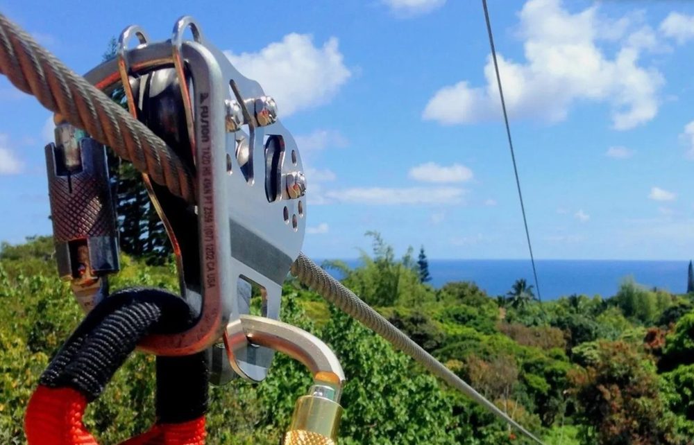 Zipline trolley and carabiner hardware on the cable, overlooking the coastline and ocean on the 8-Line Zipline Eco Tour