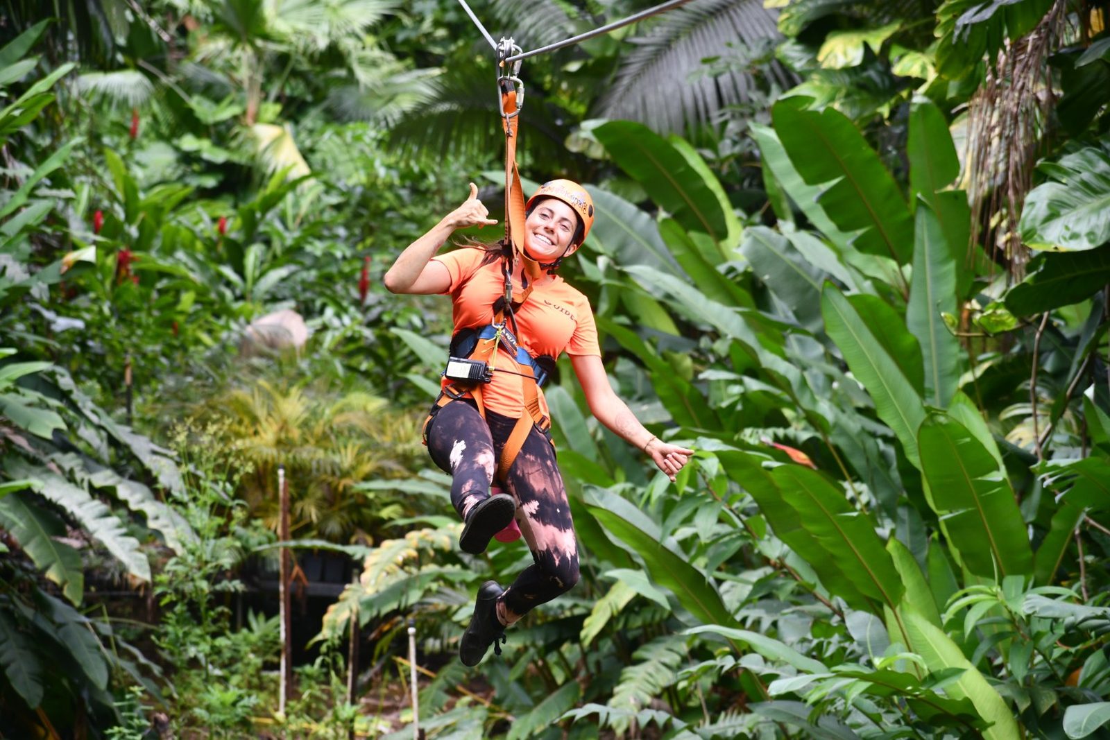 Guide flashing a shaka while ziplining through the lush jungle canopy on the 8-Line Zipline Eco Tour, Maui
