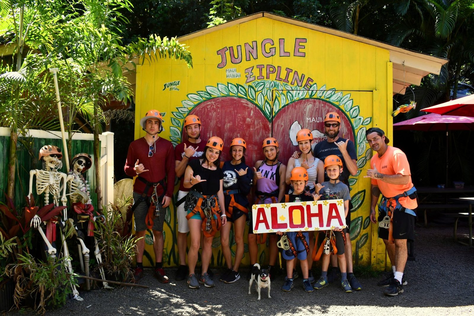 Group of guests in helmets holding an Aloha sign in front of the Jungle Zipline basecamp, Maui
