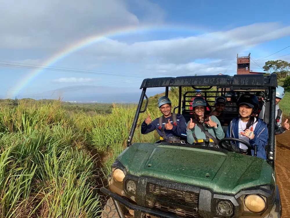 Group of guests giving a thumbs up from an ATV as a full rainbow arcs over the green hillside on the ride-along portion of the tour.